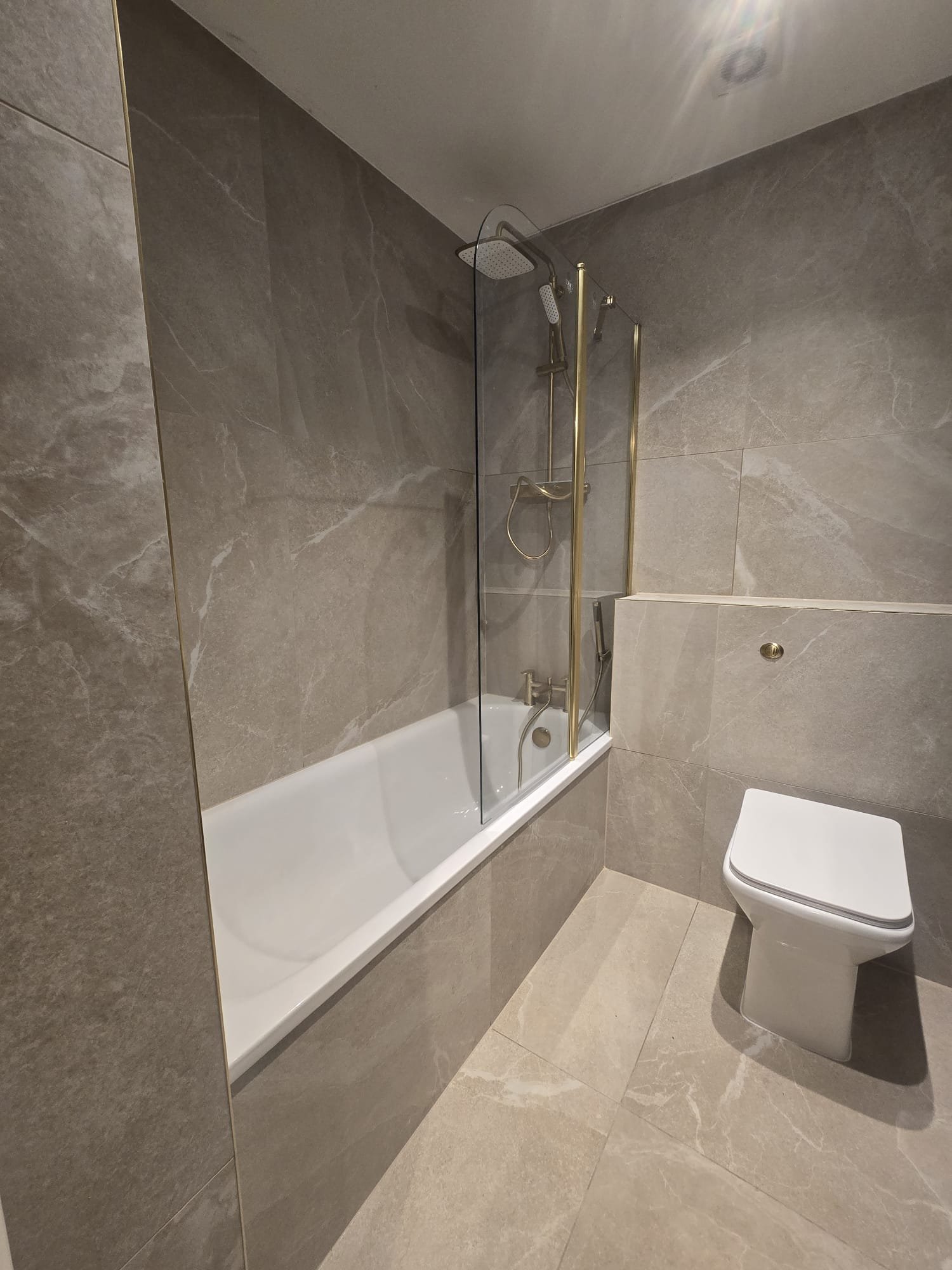 https://fixandflip.sdsdigitalsolutions.com/wp-content/uploads/2026/08/grey-tiled-bathroom-glass-screen-bath.jpg